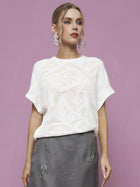 A woman stands against a pink background, wearing the Social Queen Cutout Jacquard Knit Top in white, paired with a gray embroidered skirt and large dangling earrings.