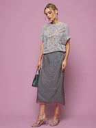 A woman poses against a pink background wearing the Social Queen Cutout Jacquard Knit Top in light gray, paired with a gray midi skirt, silver heels, and carrying a small dark handbag.