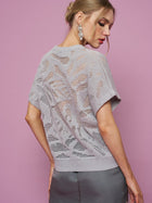 Woman with blonde hair in an updo wears dangly earrings, a Social Queen Cutout Jacquard Knit Top in light purple, and a dark skirt, standing against a pink background.