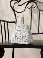 The Social Queen Cutout Leather Top-Handle Mini Bag, featuring a white geometric design, sits on a black wooden chair with a decorative metal backrest.