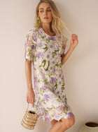 A woman models the Social Queen Dimensional Embroidered Beaded Lace Dress in purple, green, and white while holding a beaded handbag against a plain wall.