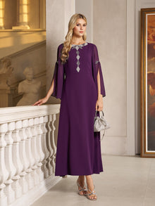 A woman in the Elegant Beaded Split-Sleeve Dress by Social Queen stands indoors by a white railing, holding a small silver handbag and wearing silver sandals.
