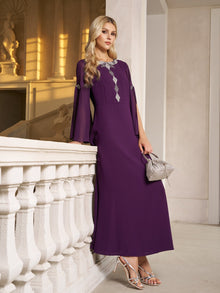 A woman wearing the Social Queen Elegant Beaded Split-Sleeve Dress stands by a white railing in a softly lit, elegant space, holding a silver handbag and wearing silver heels.