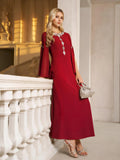 A woman in the Social Queen Elegant Beaded Split-Sleeve Dress with silver accents leans against a white railing, holding a silver handbag and wearing silver heels in an elegant indoor setting.