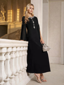 A woman stands by a white railing in an elegant indoor setting, wearing the Social Queen Elegant Beaded Split-Sleeve Dress, paired with silver heels and a small silver handbag.