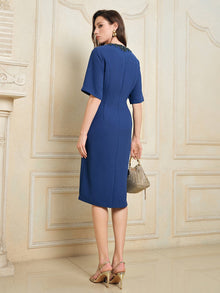 A woman in the Social Queen Elegant Hand-Beaded Green Crystal Dress stands indoors, facing away and holding a textured handbag, paired with heeled sandals.