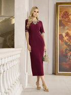 A woman stands indoors near a railing and a large painting, wearing the Social Queen Elegant Rhinestone-Embellished Dress and holding a small handbag.