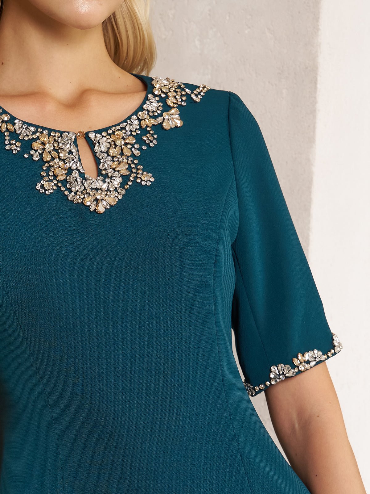 A woman wears the Social Queen Elegant Rhinestone-Embellished Dress, a fitted teal sheath in chiffon with intricate rhinestone details at the neckline and sleeve cuffs.