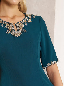 A woman wears the Social Queen Elegant Rhinestone-Embellished Dress, a fitted teal sheath in chiffon with intricate rhinestone details at the neckline and sleeve cuffs.