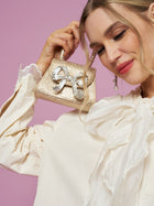 A woman in the Social Queen Embroidered Cutout Bow-Tie Blouse holds a small, glittery gold handbag with a decorative silver bow against a pink background.