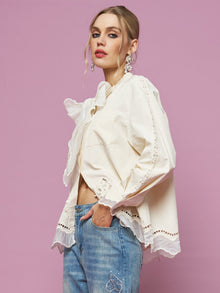 A woman models the Social Queen Embroidered Cutout Bow-Tie Blouse with blue jeans, standing in front of a light pink background and looking at the camera.