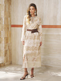 A woman stands indoors in the Social Queen Embroidered Fringe Lace Crystal-Trimmed Dress with long sleeves, a brown belt, and black heeled sandals—an elegant, neutral look ideal for wedding guests.