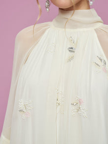 A person wearing the Embroidered High-Neck Silk Dress by Social Queen, styled with pearl earrings, set against a pink background.