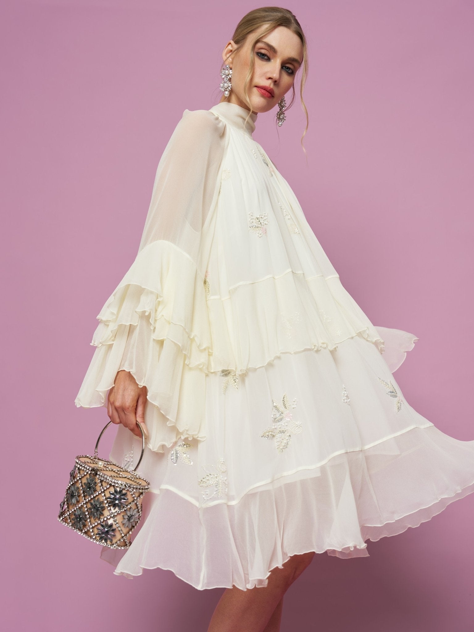 A woman poses against a purple background in the Social Queen Embroidered High-Neck Silk Dress, styled with a small embellished handbag and statement earrings.