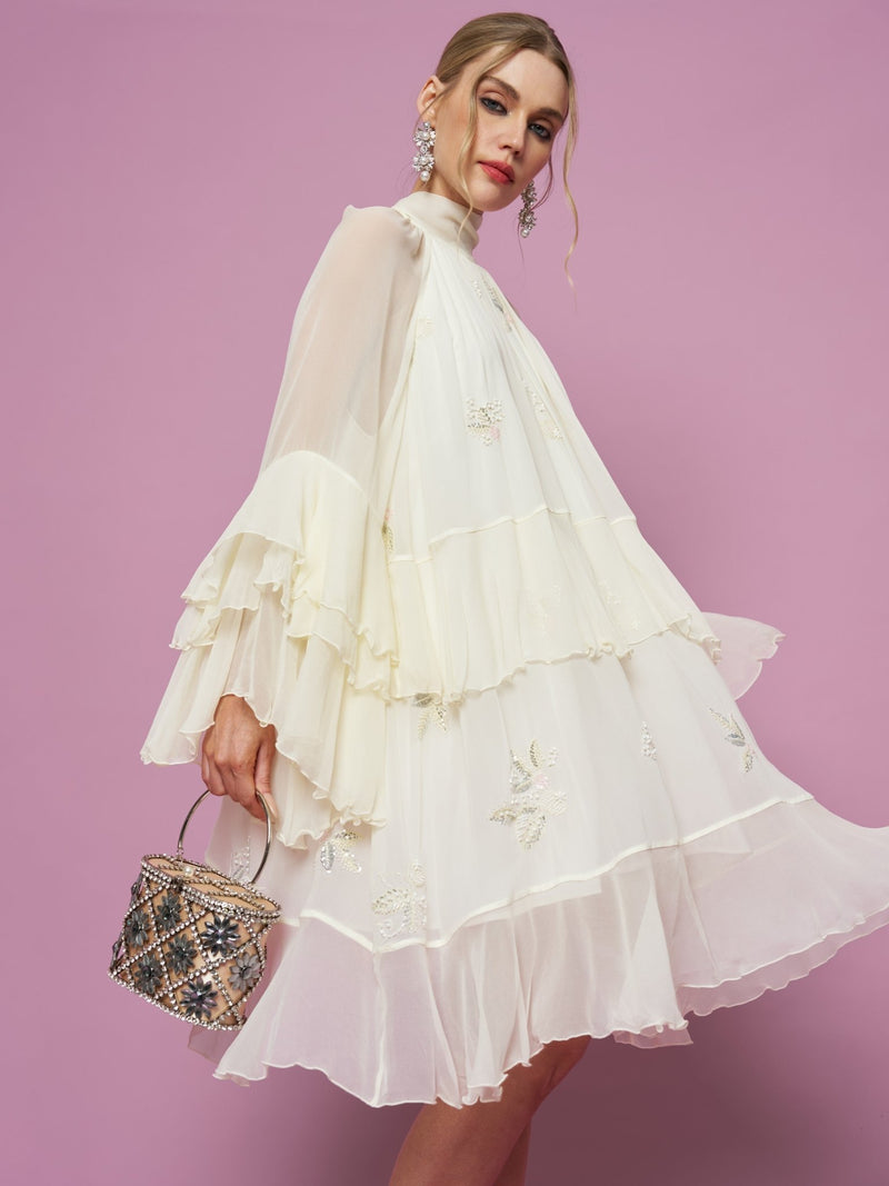 A woman poses against a purple background in the Social Queen Embroidered High-Neck Silk Dress, styled with a small embellished handbag and statement earrings.