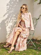 A woman in a Social Queen Embroidered Jacquard Ruffle Lace-Trim Dress sits outdoors on a green metal chair, wearing sunglasses and heeled sandals, and holding a small floral handbag.