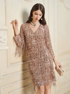 A woman wearing the Social Queen Embroidered Sequin Tassel Mini Dress in a neutral tone holds a clutch while standing against an ornate, light-colored wall.