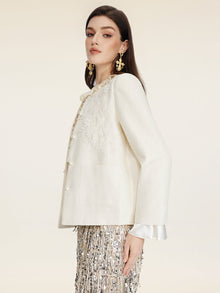 A woman in profile wears Social Queen's Embroidered Wool Jacket with Pearl Accents over a white ruffled blouse, styled with a metallic fringe skirt and gold statement earrings against a plain background.