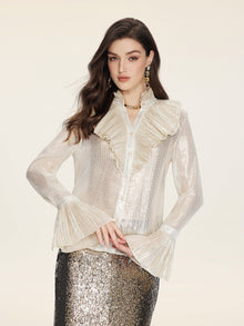 A woman wears the Social Queen Ethereal Metallic Ruffle Silk Blouse, featuring sheer silk with gold threads and a ruffled high collar, paired with a silver sequin skirt, against a plain light background.