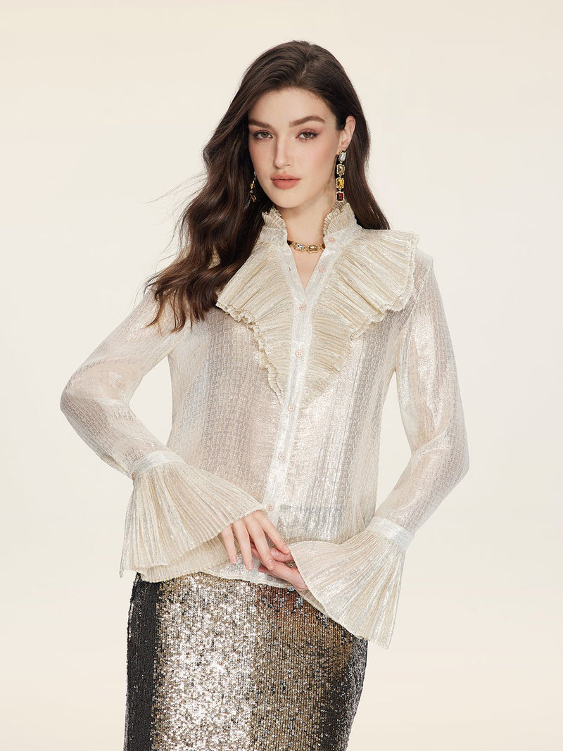 A woman wears the Social Queen Ethereal Metallic Ruffle Silk Blouse, featuring sheer silk with gold threads and a ruffled high collar, paired with a silver sequin skirt, against a plain light background.