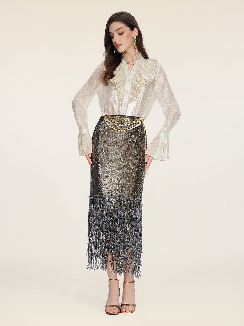 A woman wears the Social Queen Ethereal Metallic Ruffle Silk Blouse, styled with layered gold belts and earrings, and a metallic sequin fringe skirt, standing against a plain light background.