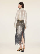 A woman stands facing away, wearing the Social Queen Ethereal Metallic Ruffle Silk Blouse, paired with a sequined fringe skirt and gold high-heeled sandals against a plain background.