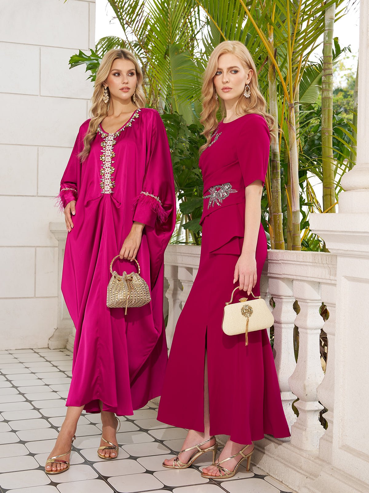 Two women in Social Queen Feather-Trimmed Embellished Satin Caftan Dresses stand by a white stone railing with green plants behind them. Each holds a small handbag and wears sandals.