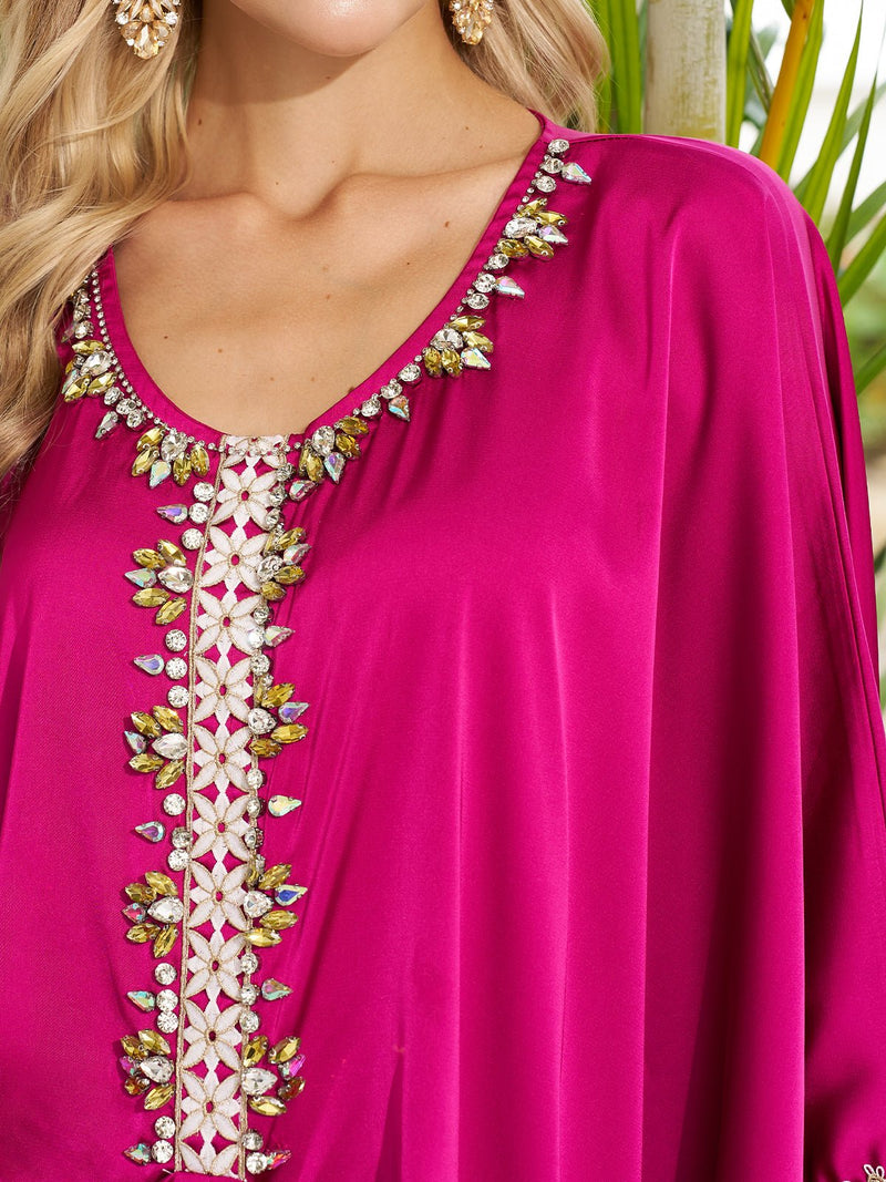 A woman stands outdoors near a green plant, wearing the Social Queen Feather-Trimmed Embellished Satin Caftan Dress.