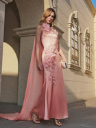 A woman in the Social Queen Floral Appliqué Satin Fishtail Gown stands outdoors by a stone building with arched windows, holding a clutch bag.