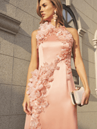 A woman stands elegantly before a stone building in the Social Queen Floral Appliqué Satin Fishtail Gown, featuring blush pink satin, 3D floral appliqués, and a sleeveless fishtail silhouette, accessorized with a small clutch.