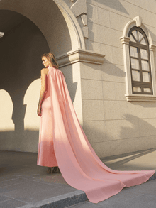 A woman wears the Social Queen Floral Appliqué Satin Fishtail Gown, featuring 3D floral details, as she stands outside a building with arched windows and beige stone walls.
