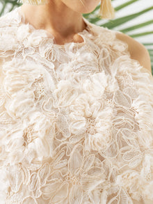 Close-up of a person wearing the Social Queen Floral Appliqué Sheer Sleeveless Top, featuring cream-colored lace, floral patterns, and 3D floral appliqué. A green leaf appears in the background.