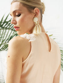 A woman wearing the Social Queen Floral Appliqué Sheer Sleeveless Top stands in front of green palm leaves, paired with large tassel earrings.