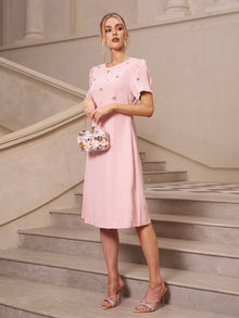 A woman stands on a staircase wearing the Social Queen Floral Beaded Puff Sleeve Dress, paired with a small floral handbag and heeled sandals.