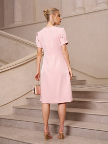 A woman in the Social Queen Floral Beaded Puff Sleeve Dress and heeled sandals stands on a staircase, facing away and holding a small matching handbag.