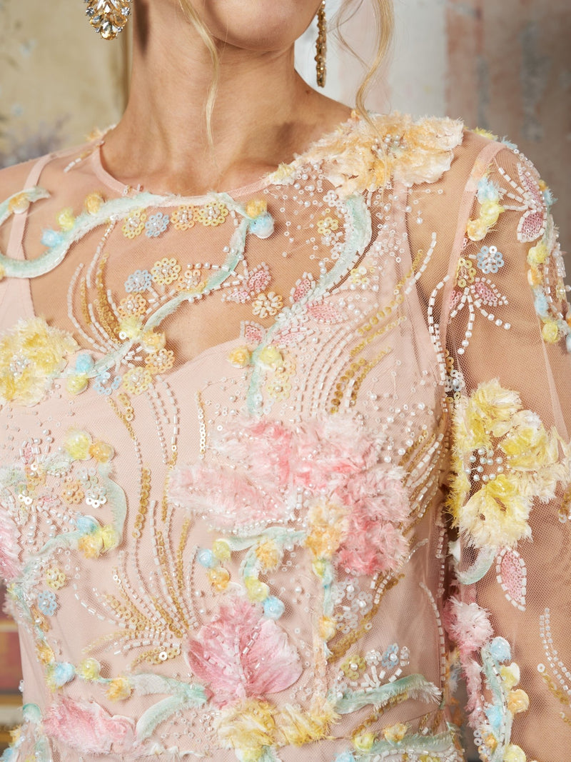 Close-up of a woman wearing the Floral Beaded Sheer Gown by Social Queen, featuring pastel pink sheer fabric with 3D floral appliqué, sequins, beading, and textured embroidery.