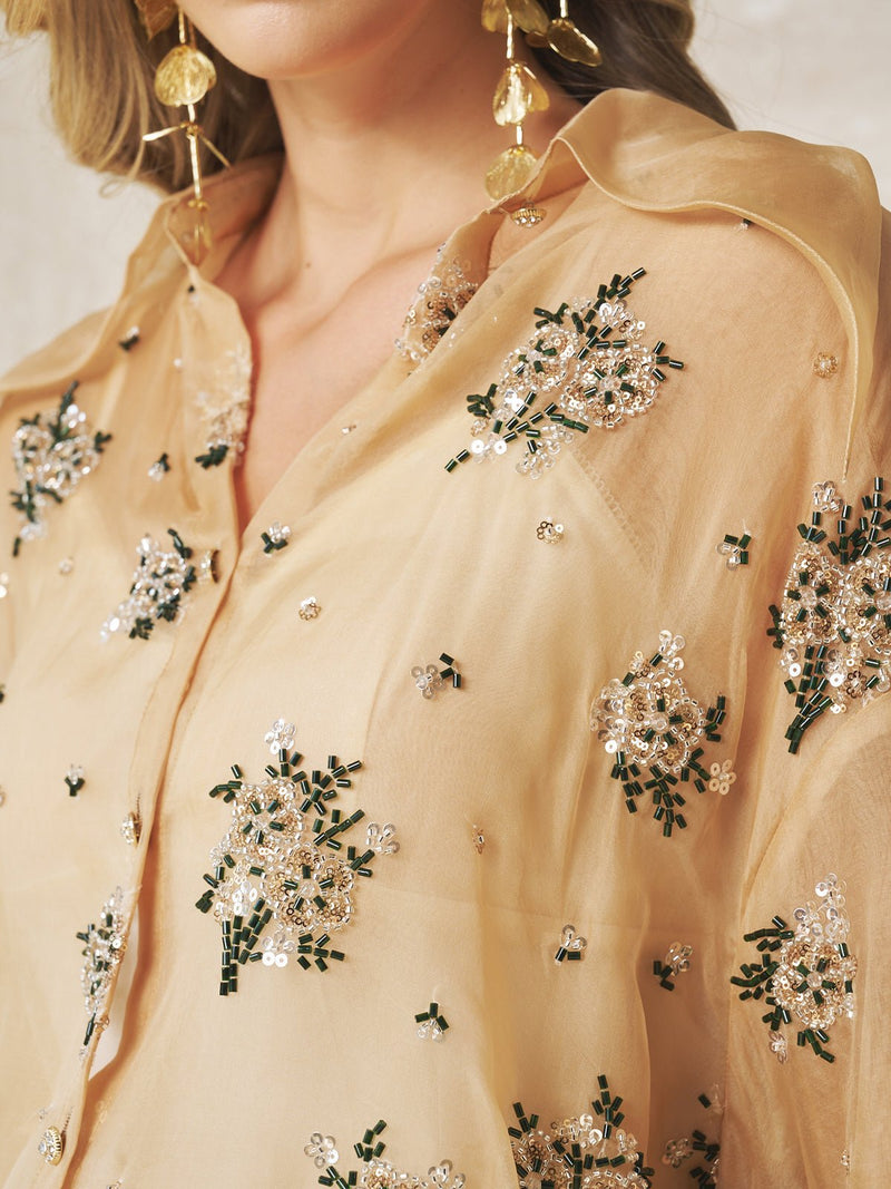 A close-up of a person wearing the Social Queen Floral Beaded Silk Blouse, featuring intricate floral bead and sequin embroidery, styled with large gold earrings and a delicate silk scarf.