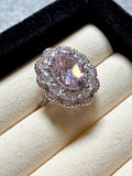 The Floral Crystal Ring by Social Queen features a pink oval gemstone surrounded by a sparkling floral halo, beautifully presented in a cream-colored ring box.
