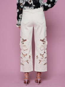Model wears Social Queen Floral Cutout High-Rise Jean in white and a black floral top, standing against a pink background, shown from the back.