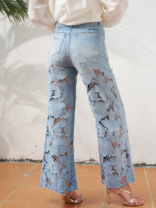 A person wearing Social Queen’s Floral Cutout Stretch Denim Jean and heeled sandals stands on a tiled floor against a white wall.