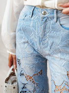 Close-up of a person wearing Social Queen's Floral Cutout Stretch Denim Jean, featuring intricate floral cutouts, while holding a white handbag in their left hand.