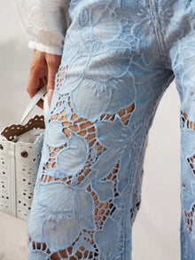 Close-up of a person wearing Social Queen Floral Cutout Stretch Denim Jean in light blue and holding a white perforated handbag.