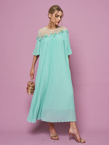 A woman wears the Social Queen Floral Embellishment Pleated Dress, featuring a loose fit and floral beadwork, holding a small handbag against a pink background. The relaxed silhouette gives her look effortless charm.