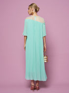 A woman faces away against a pink background, wearing the Social Queen Floral Embellishment Pleated Dress in light blue with a relaxed silhouette, paired with pink heels and a small gold and white handbag.