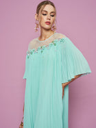 A woman poses against a pink background wearing the Social Queen Floral Embellishment Pleated Dress, styled with statement earrings and a small purse.