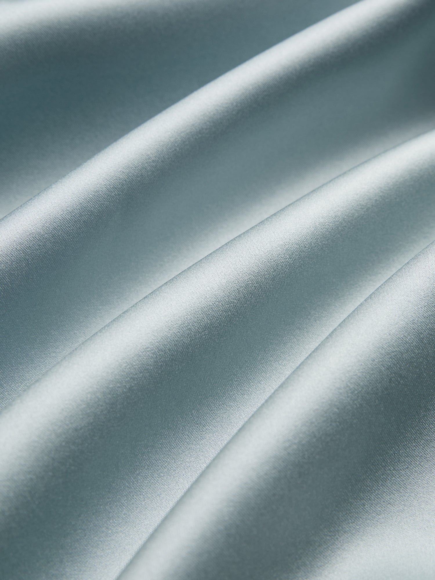 Close-up of smooth, light blue satin fabric with gentle folds and a shiny finish, evoking the Social Queen Floral Embroidered Beaded Jacket accented with hand-embroidered floral motifs.