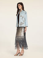 A woman stands in profile against a plain background wearing the Social Queen Floral Embroidered Beaded Jacket, a black top, a silver sequin fringe skirt, and gold high-heeled sandals.