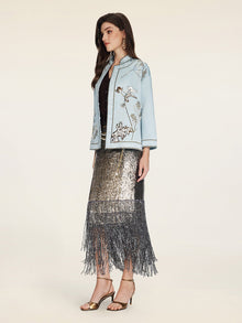 A woman stands in profile against a plain background wearing the Social Queen Floral Embroidered Beaded Jacket, a black top, a silver sequin fringe skirt, and gold high-heeled sandals.