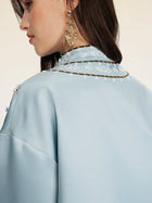 A woman wearing the Social Queen Floral Embroidered Beaded Jacket in light blue is shown from the side and back, highlighting its stand collar, hand-embroidered floral motifs, and her gold dangling earring.