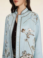 A woman, shown from the shoulders up, wears Social Queen’s Floral Embroidered Beaded Jacket in light blue with hand-embroidered motifs over a black top and gold earrings.